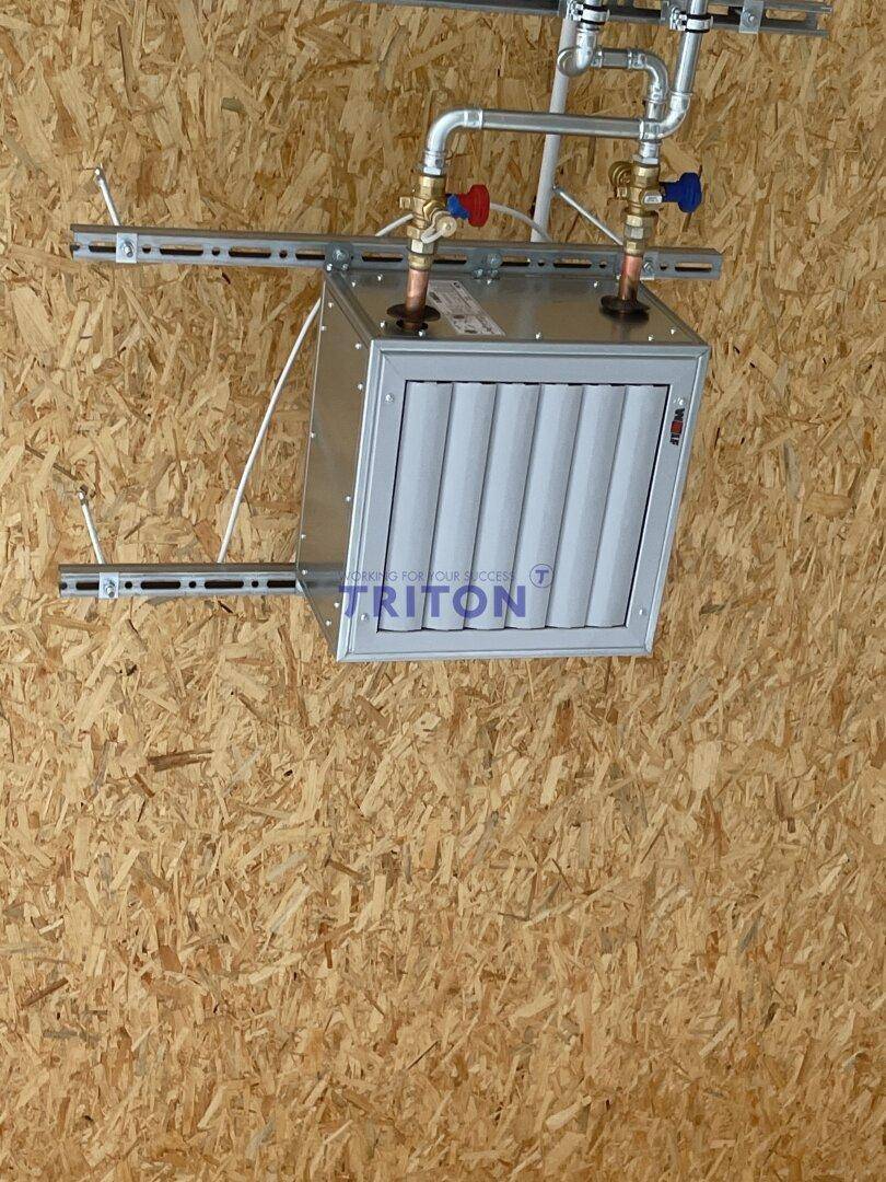 Detailansicht einer Lüftungsanlage mit Rohren und Ventilen, montiert an einer Holzdecke.