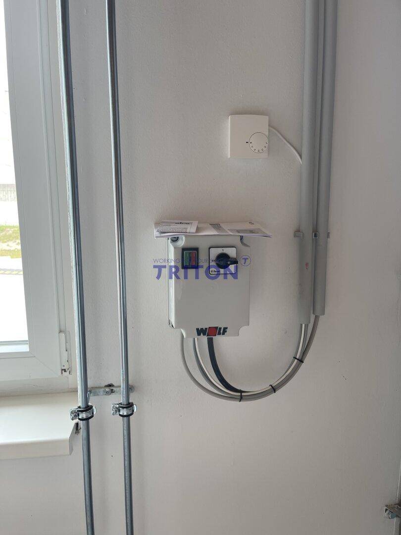 Elektrische Installationen und Leitungen an einer weißen Wand neben einem Fensterrahmen.
