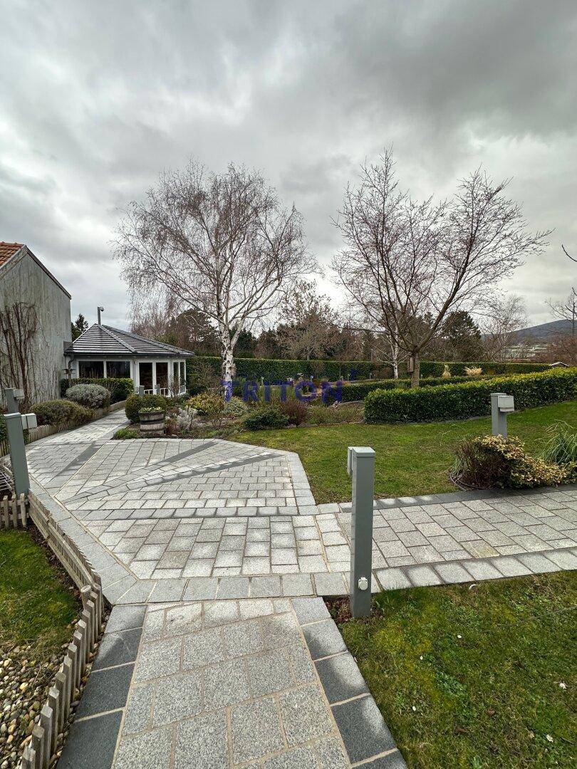 Weitläufiger Gartenbereich mit gepflasterten Wegen, Rasenflächen und einem charmanten Pavillon.