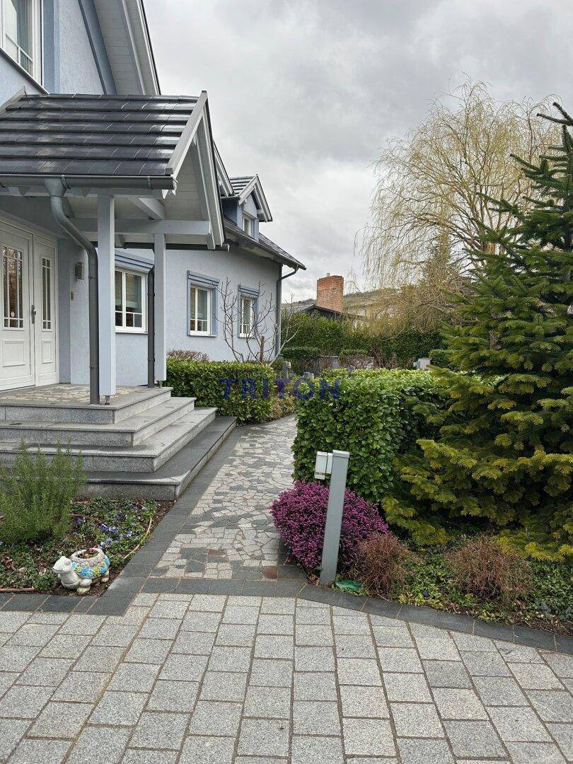 Eingangsbereich eines Hauses mit gepflastertem Weg, Stufen und gepflegten Hecken.