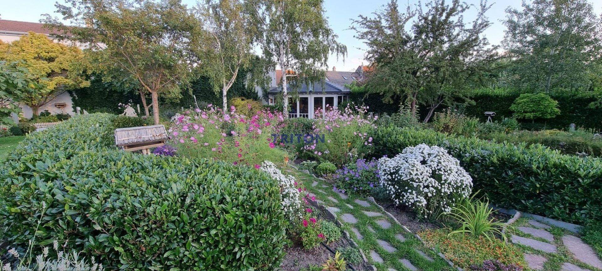Blühender Garten mit vielfältigen Pflanzen, Sträuchern und einem malerischen Steinpfad zum Haus.