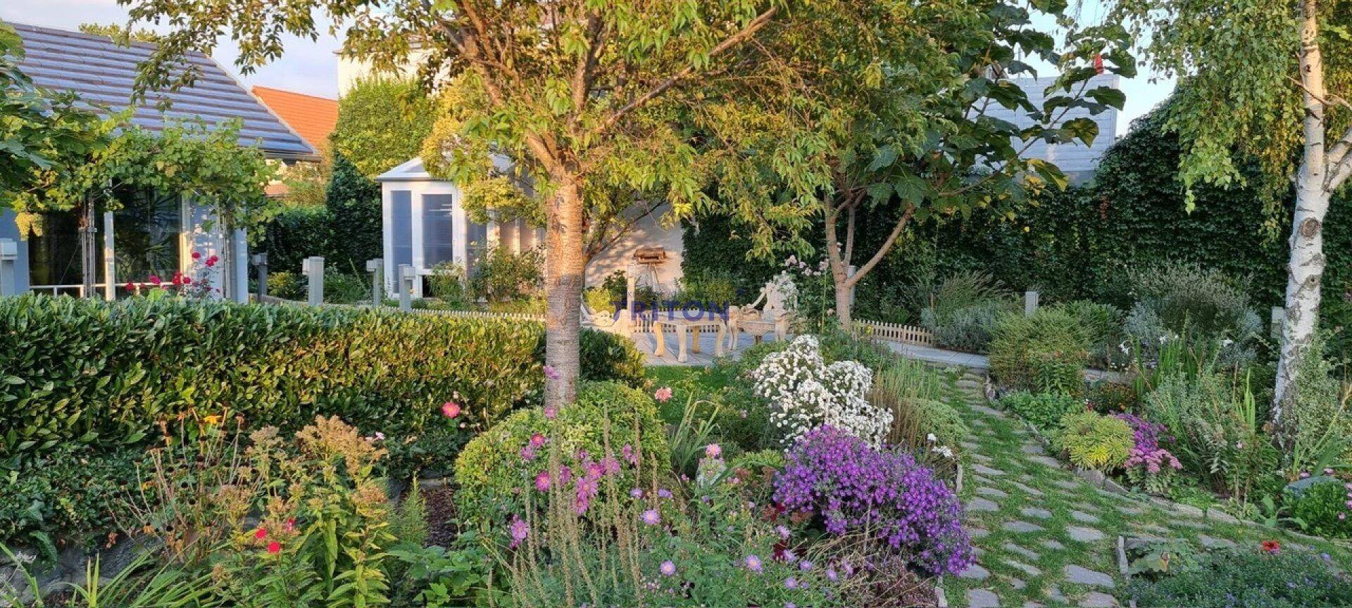 Gepflegter Garten mit blühenden Blumen, Bäumen und einem charmanten Sitzbereich im Freien.