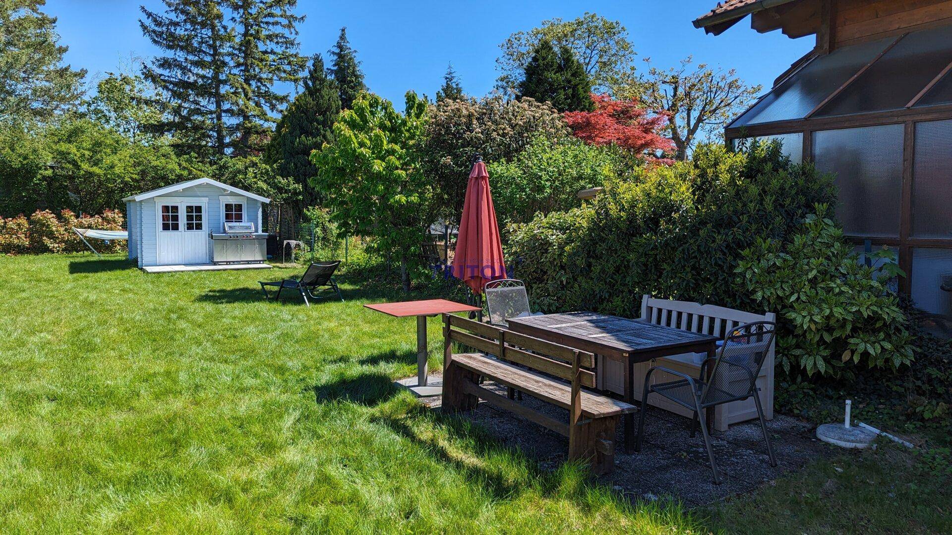 Gemütlicher Garten mit Esstisch im Freien, Sonnenschirm und Gartenhaus, ideal für entspannte Stunden.