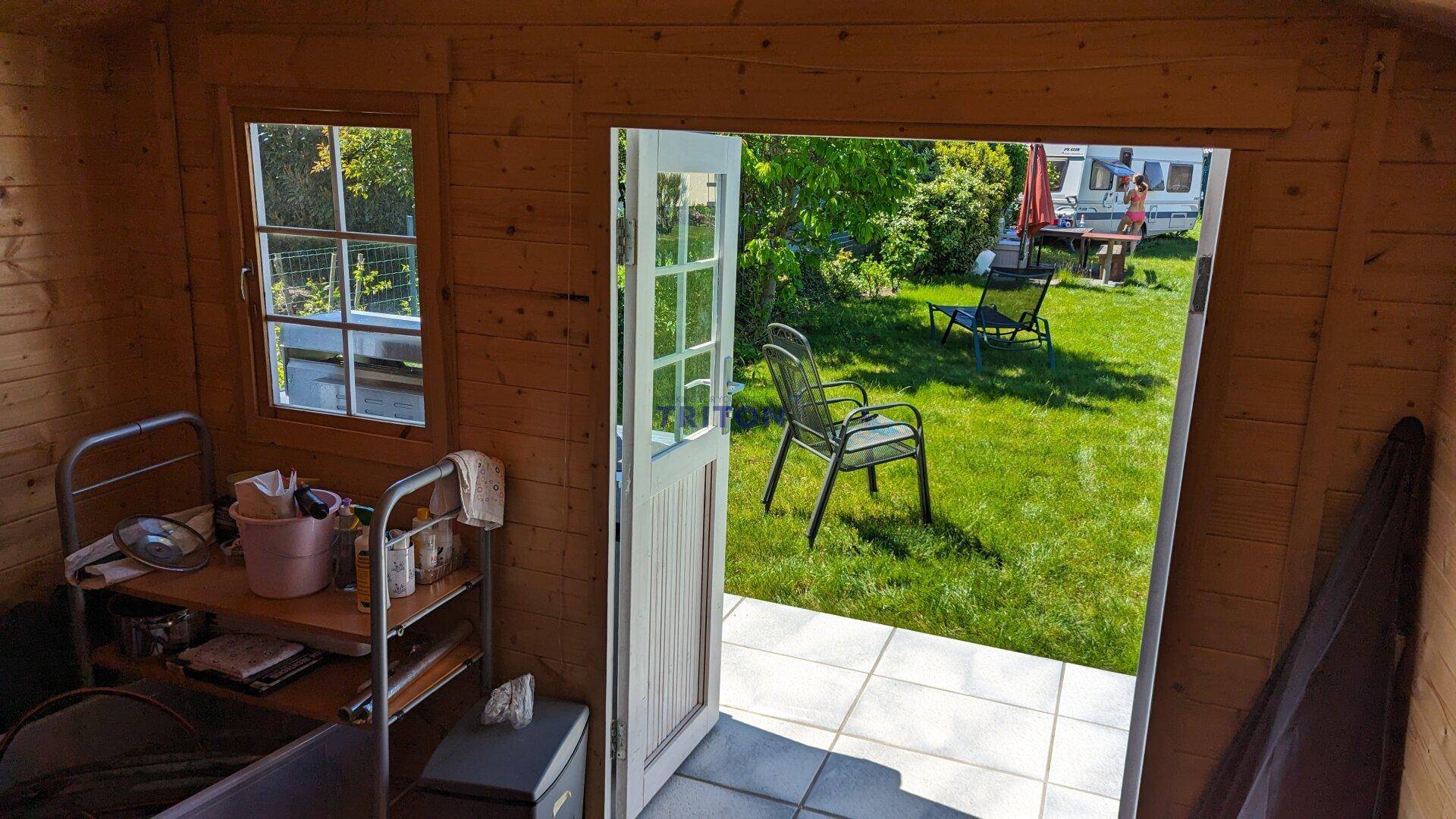 Rustikales Holz-Gartenhaus mit Blick auf die geflieste Terrasse und den grünen Garten.