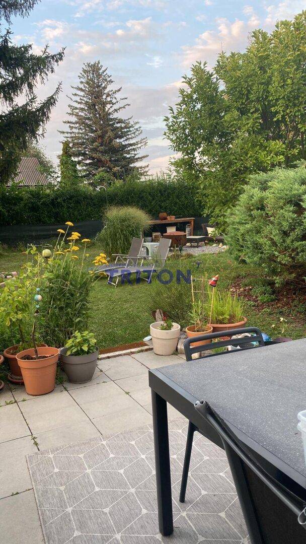 Terrasse mit Liegestühlen und Blick auf den weitläufigen Garten mit Blumenbeeten.