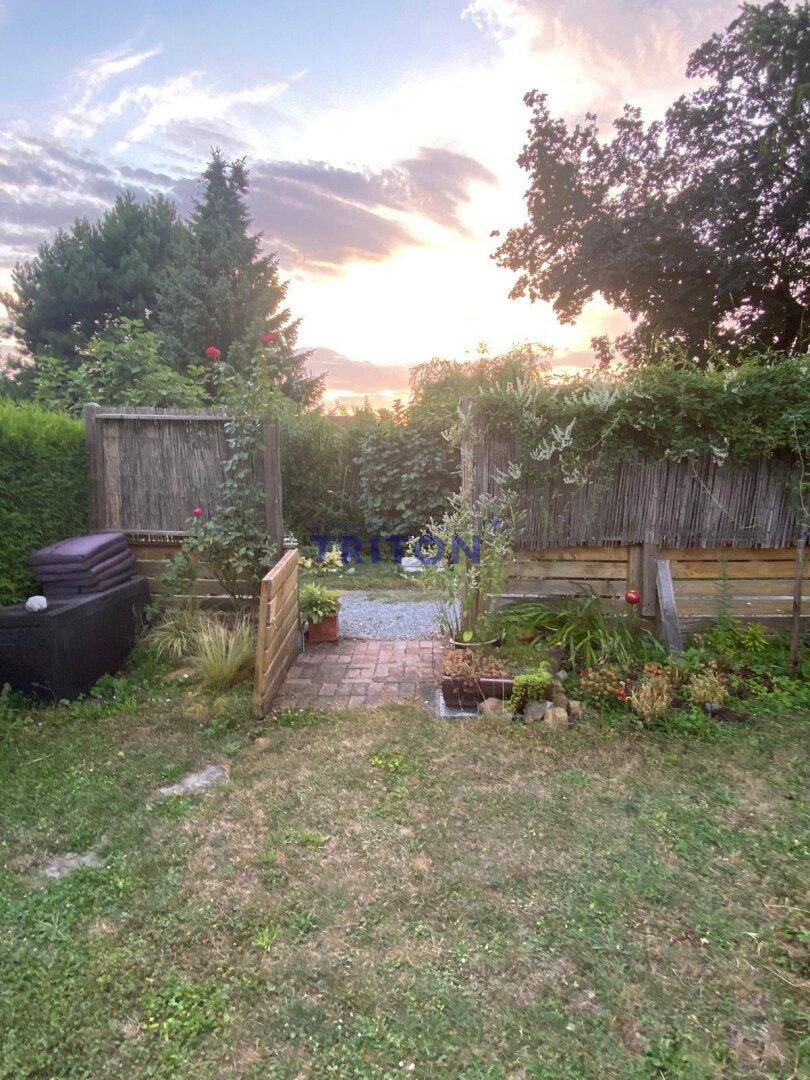 Eingangsbereich zum Garten mit Holzzaun und blühenden Rosen unter einem stimmungsvollen Abendhimmel.