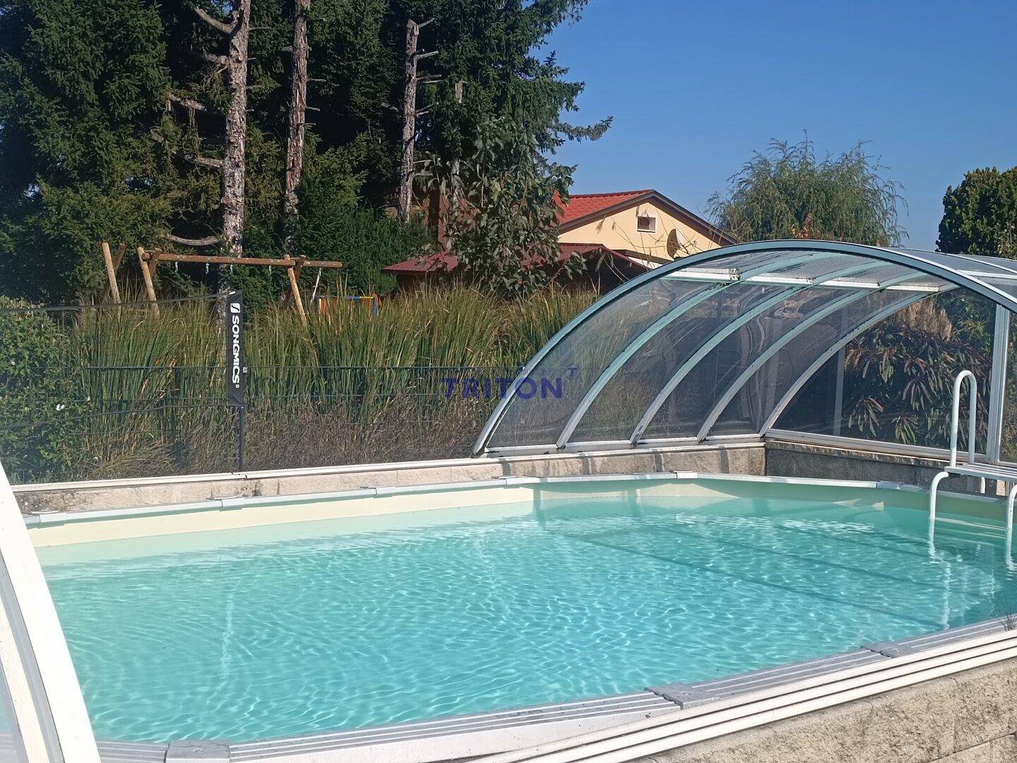 Blick auf den Außenpool mit transparenter Überdachung und Spielplatz im Hintergrund.