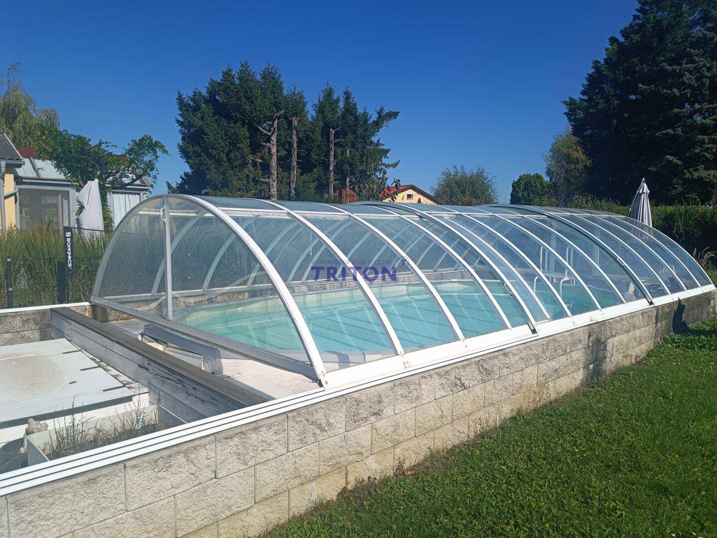 Überdachter Außenpool mit Steinumrandung und klarem Wasser unter blauem Himmel.