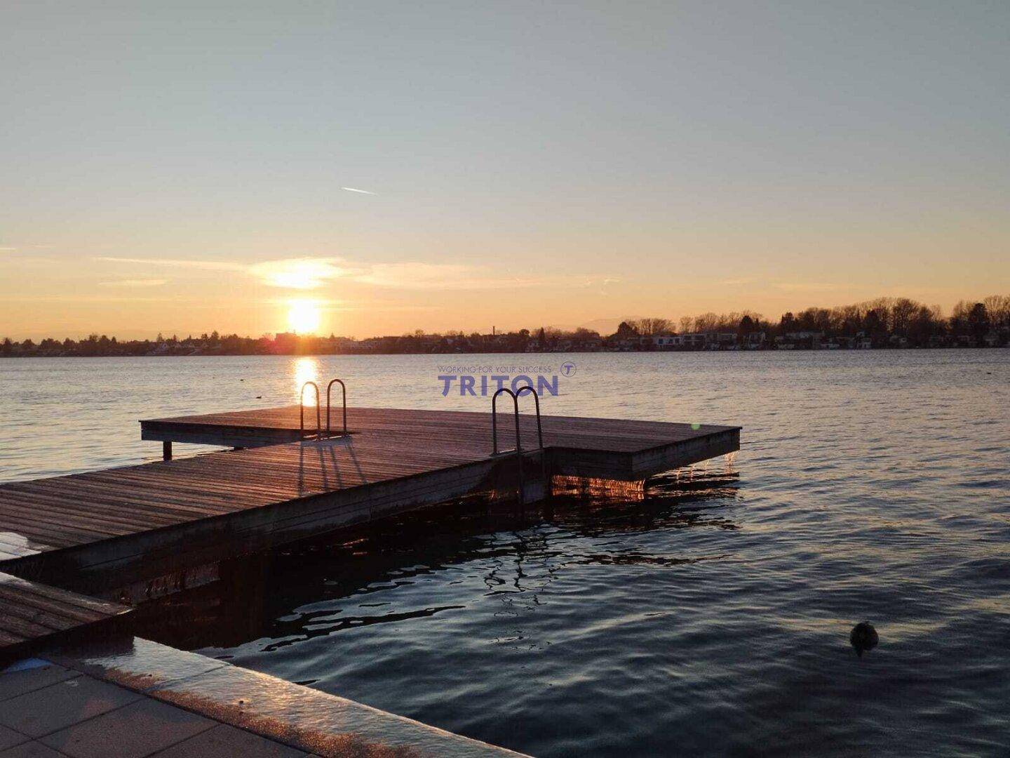 Malerischer Sonnenuntergang über einem See mit Holzsteg und Badeleiter.