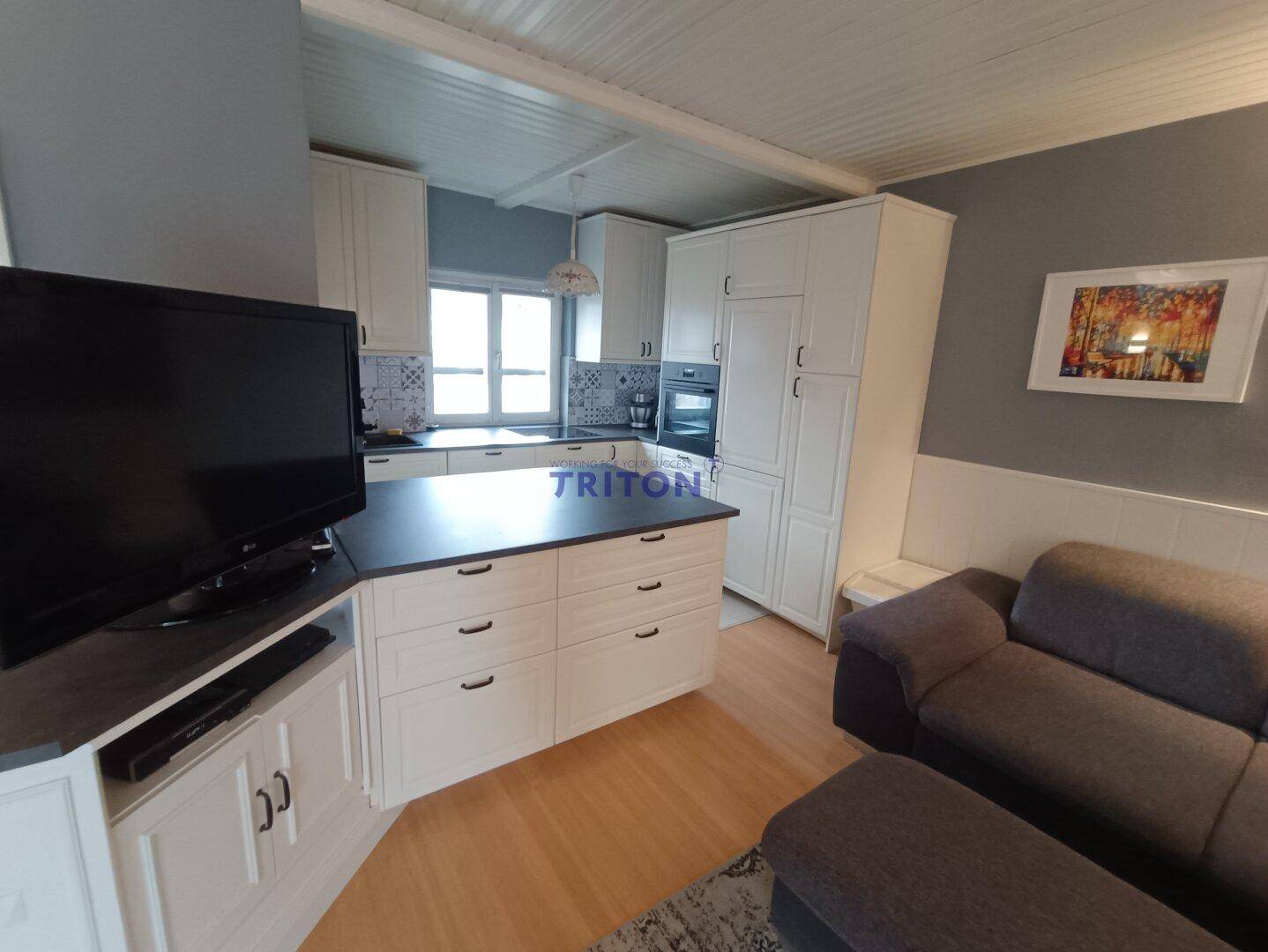 Helle Küche mit weißen Einbauschränken und angrenzendem Wohnbereich mit Sofa.