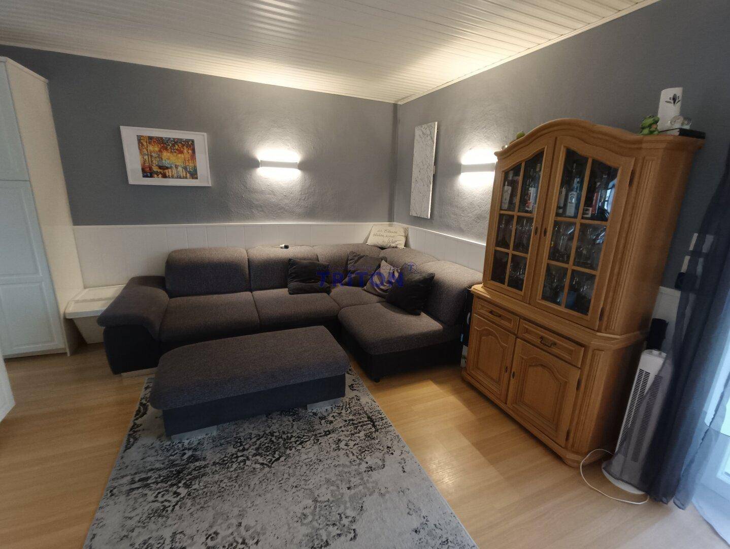 Geräumiges Wohnzimmer mit Ecksofa, Holzboden und traditionellem Holzschrank.
