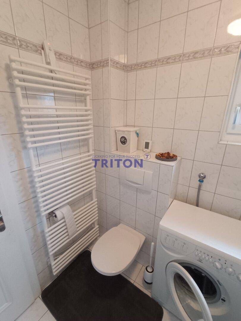 Badezimmer mit Toilette, Waschmaschine und beheiztem Handtuchhalter.