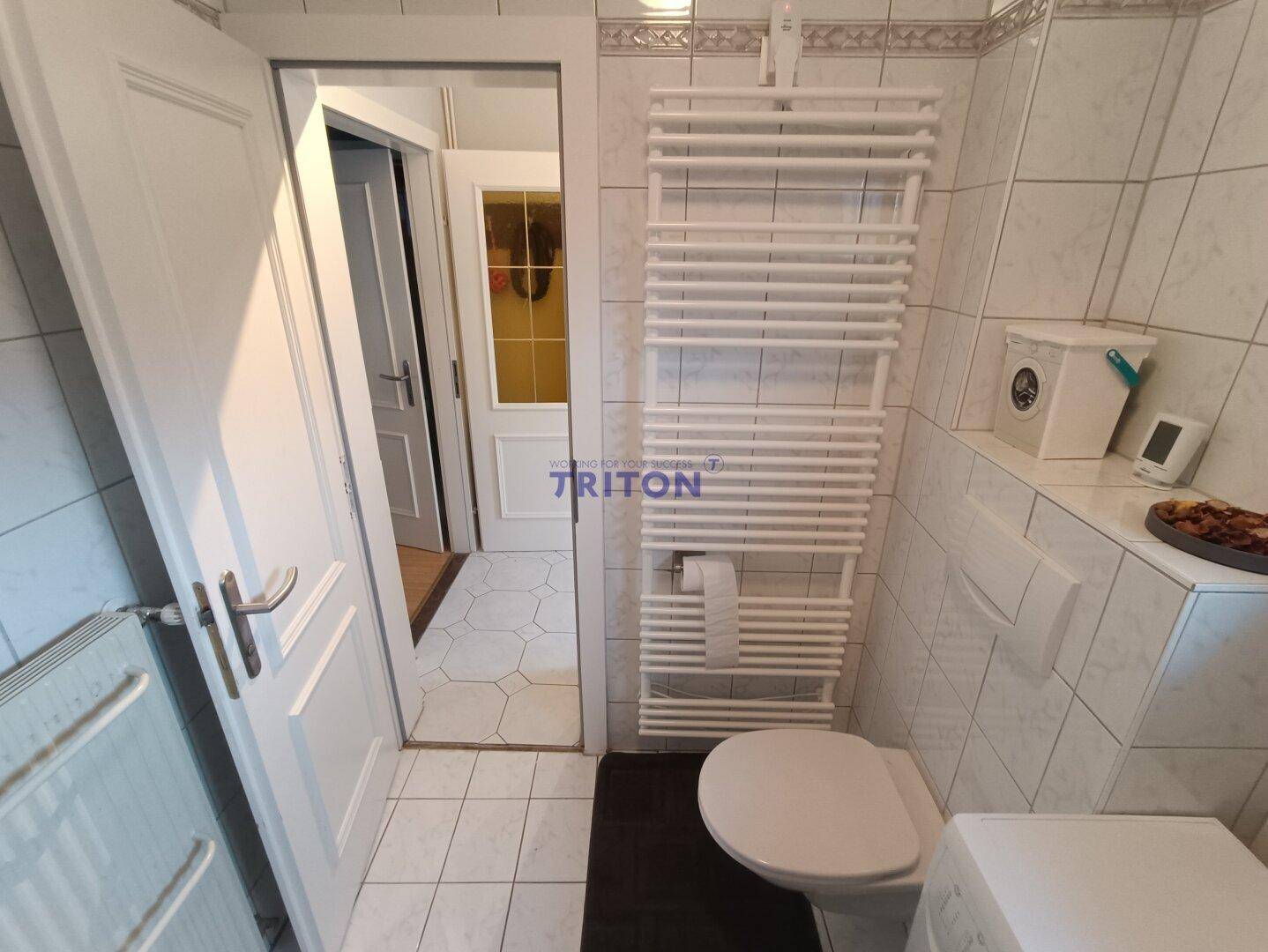 Badezimmer mit Fliesenboden und Zugang zum Flur, ausgestattet mit Heizkörper.
