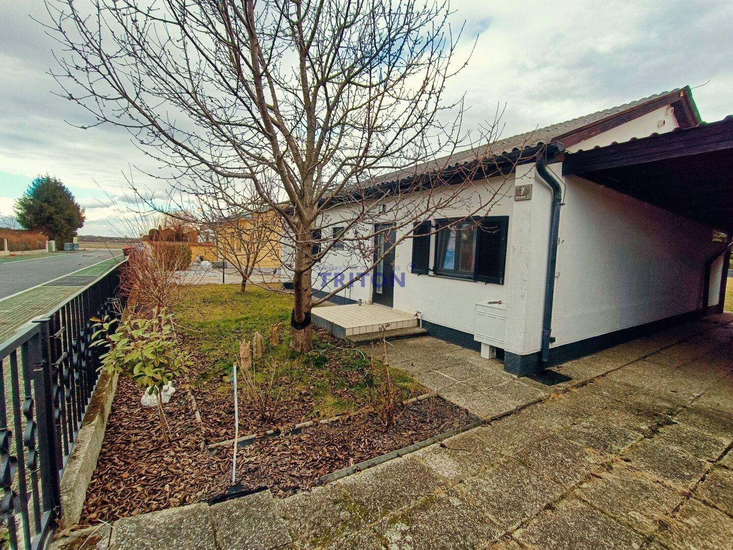Seitenansicht des Hauses mit Zufahrt, Carport und kleinem Vorgartenbereich.
