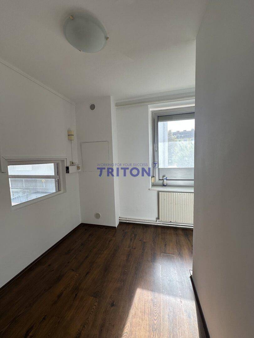 Kleiner Raum mit Laminatboden, einem Fenster zur Außenseite und einem Heizkörper darunter.