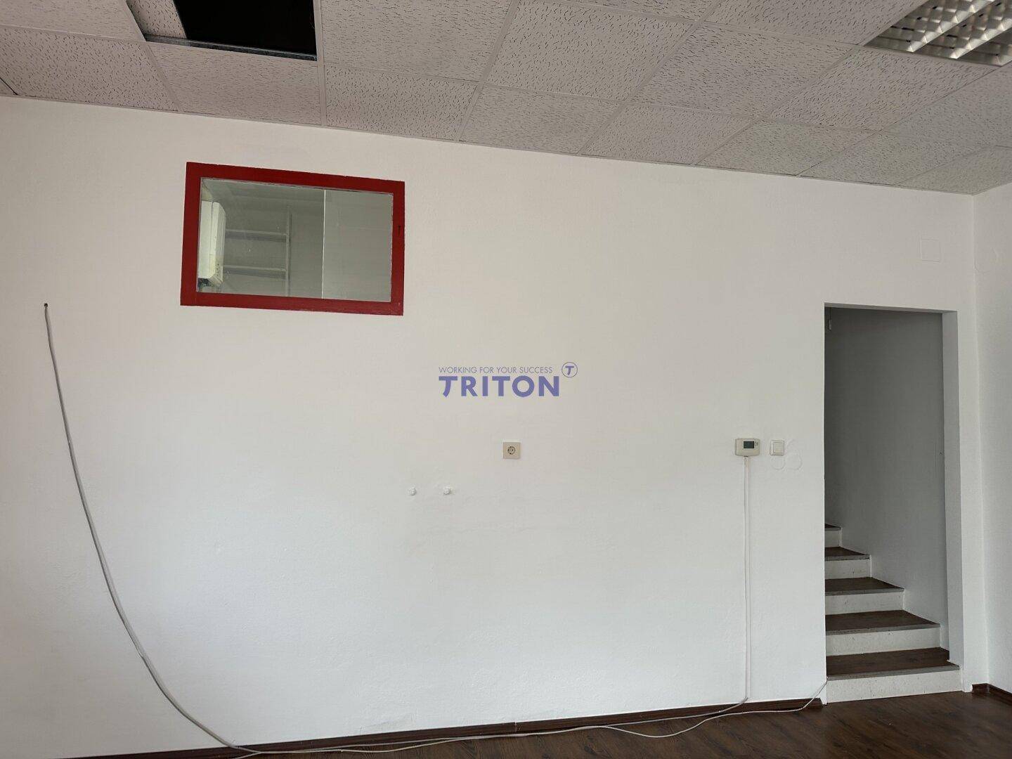 Detailansicht einer weißen Wand im Gewerberaum mit einem roten Spiegelrahmen und dem Eingang zur Treppe.