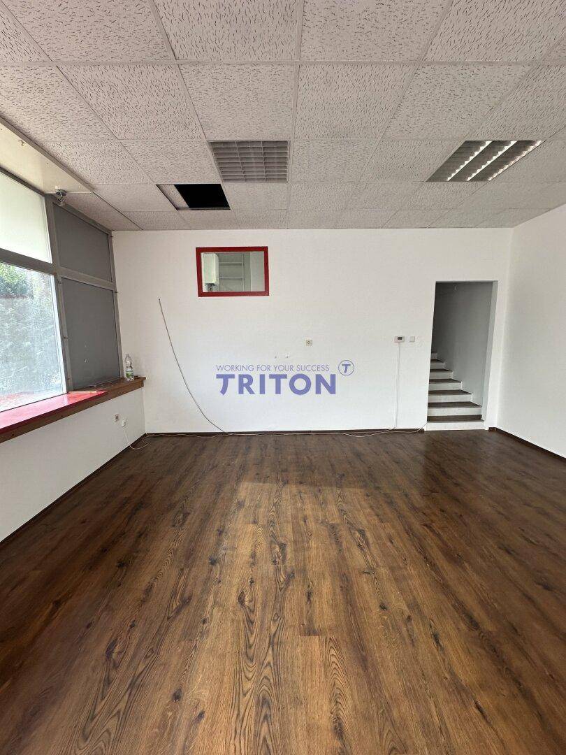 Leerer Gewerberaum mit weiß gestrichenen Wänden, Laminatboden und einem Durchgang zu einer Treppe.