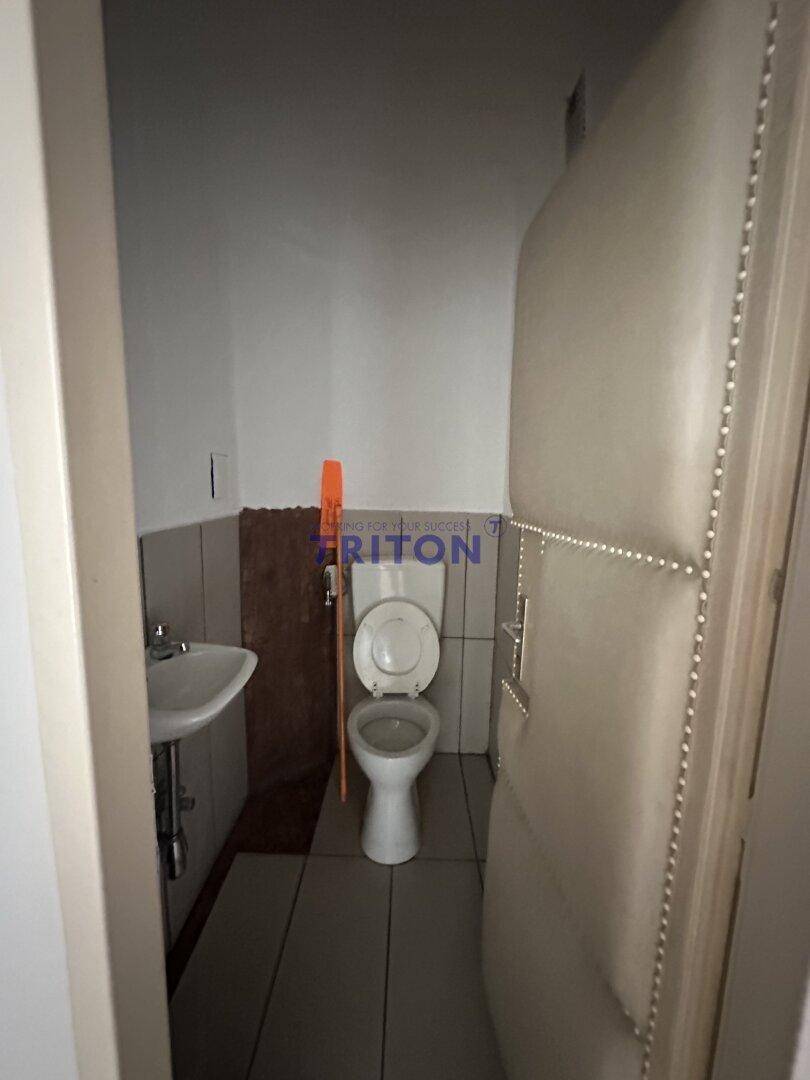 Kleiner Toilettenraum mit WC, Waschbecken und gefliestem Boden, ausgestattet mit einer gepolsterten Tür.