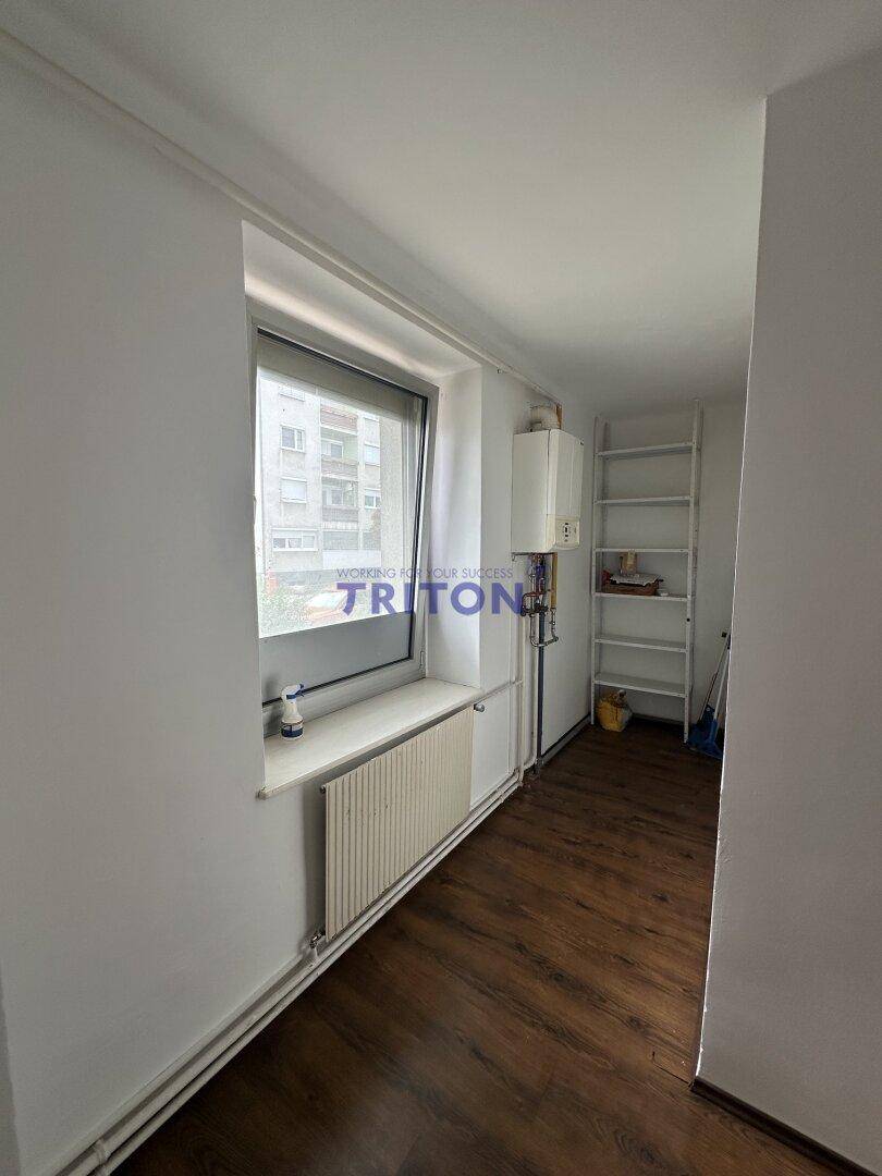 Kleiner Hauswirtschaftsraum mit Fenster, Heizkörper und einem an der Wand montierten Warmwasserbereiter.