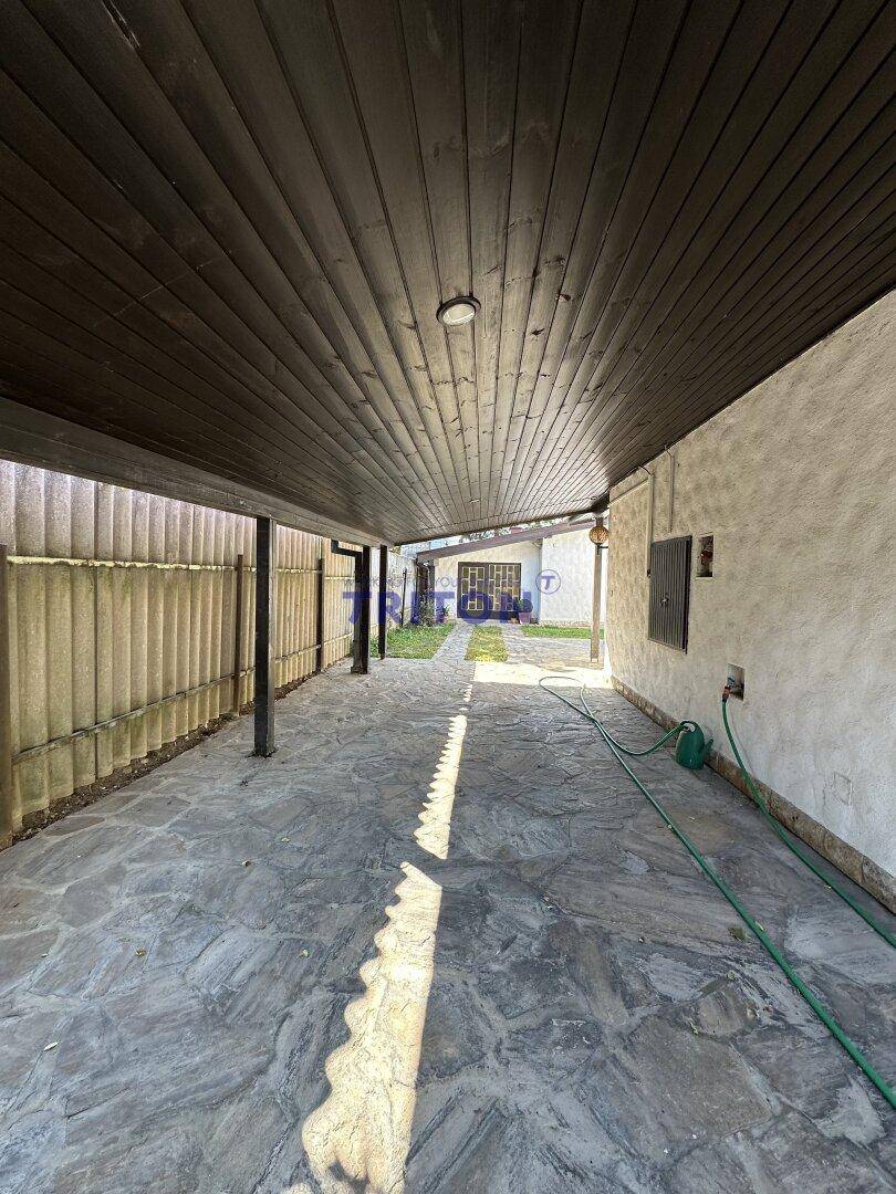 Langer überdachter Carport mit Steinplattenboden und Blick zum hinteren Gartenbereich.