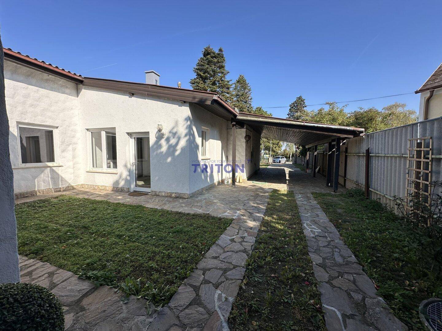Vorderansicht des Hauses mit Rasenfläche, gepflasterter Auffahrt und Carport.