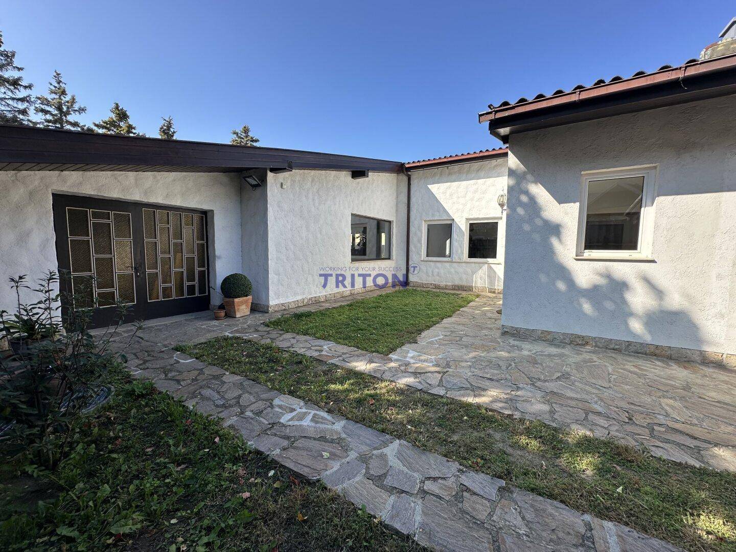 Vorderseite des Hauses mit Garage, Rasenfläche und gepflastertem Weg unter blauem Himmel.