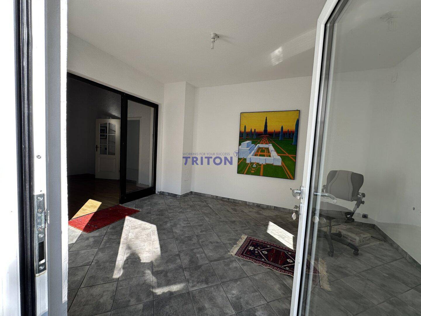 Heller Raum mit grauen Fliesen, großem Fenster und einem modernen Kunstwerk an der Wand.