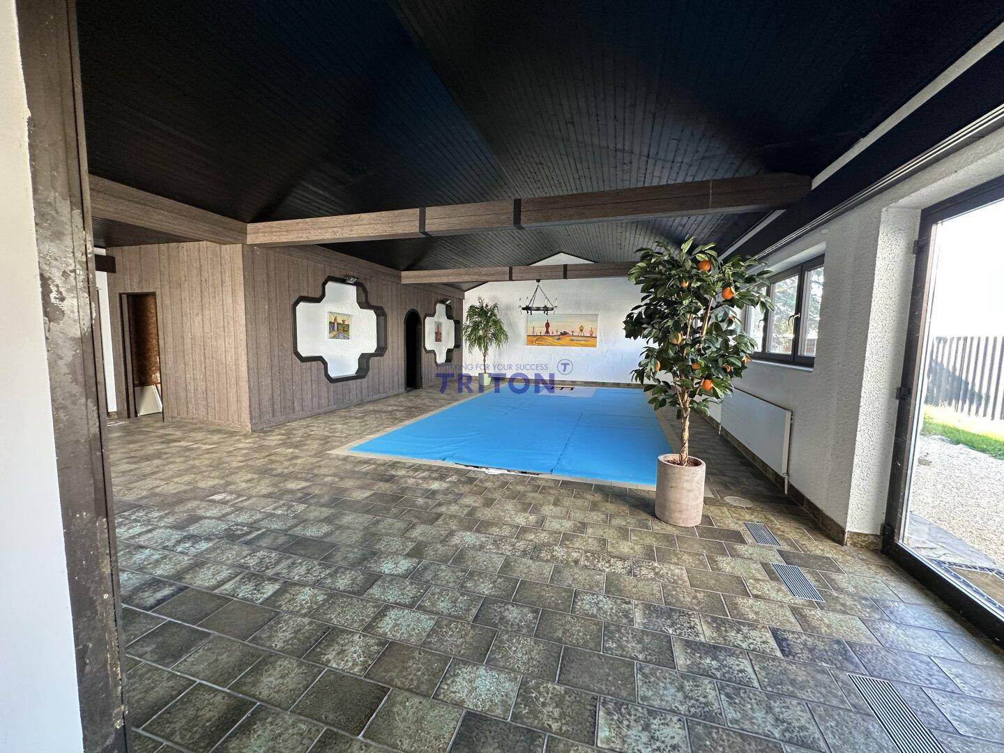 Großer Innenraum mit überdachtem Pool, Fliesenboden und Holzverkleidung an den Wänden.