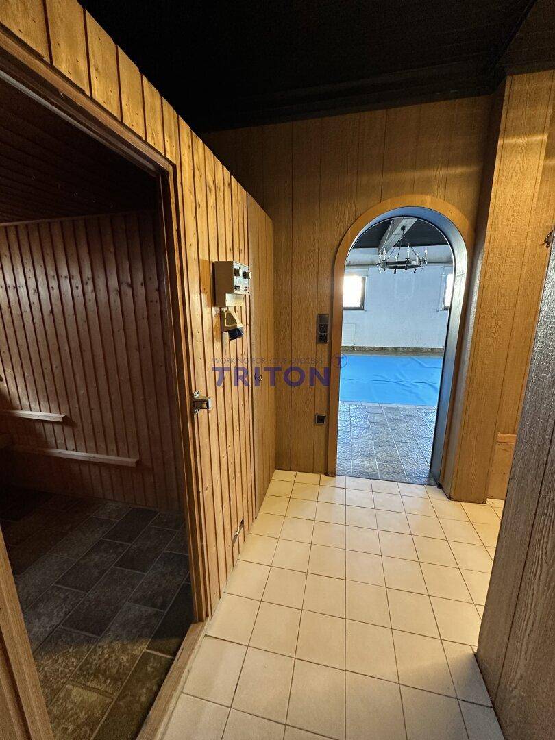 Flur mit Holzvertäfelung, weißen Fliesen und Zugang zu Sauna und Poolbereich.