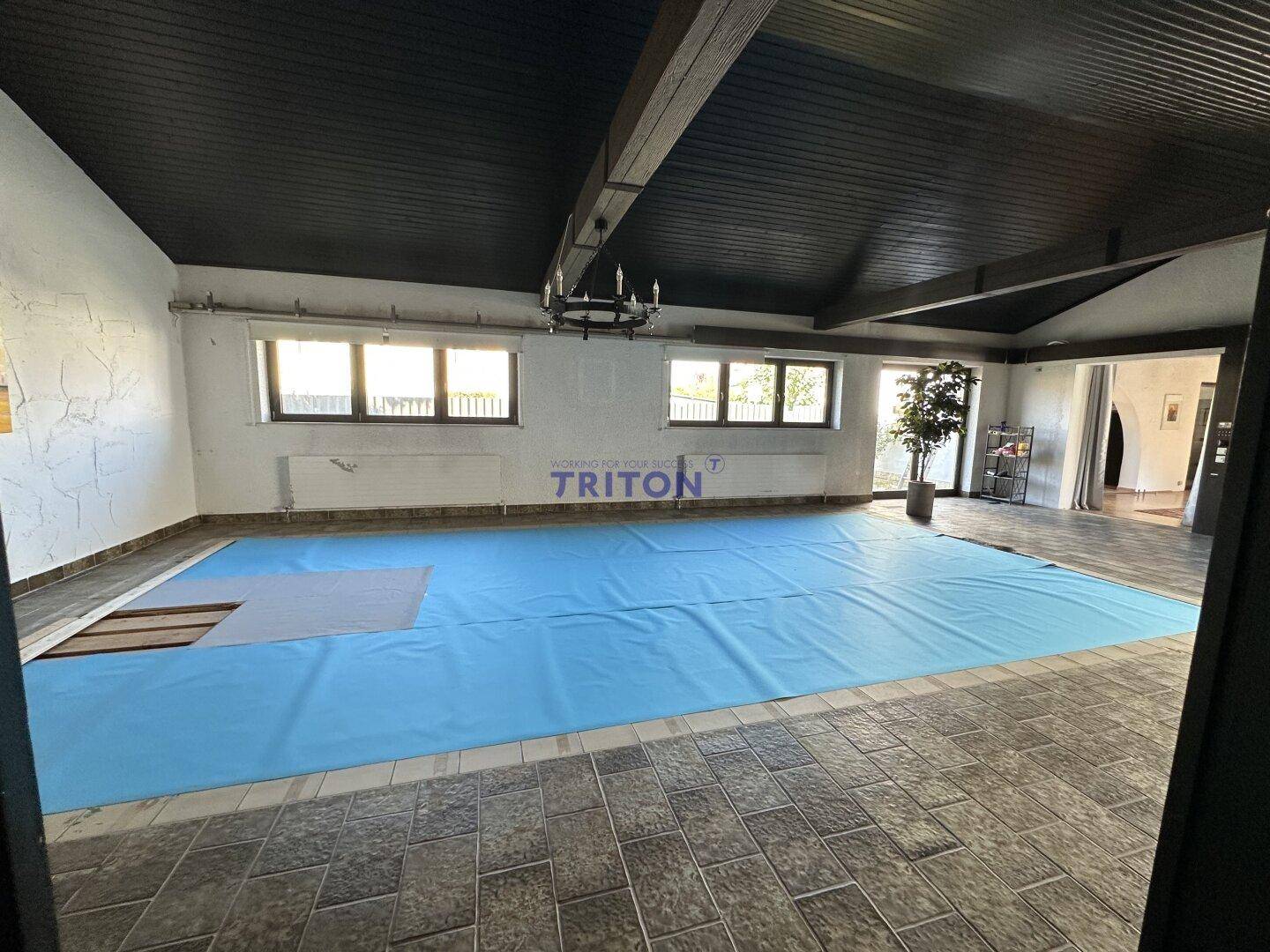Geräumiger Innenbereich mit abgedecktem Schwimmbecken, dunkler Holzdecke und rustikalem Kronleuchter.