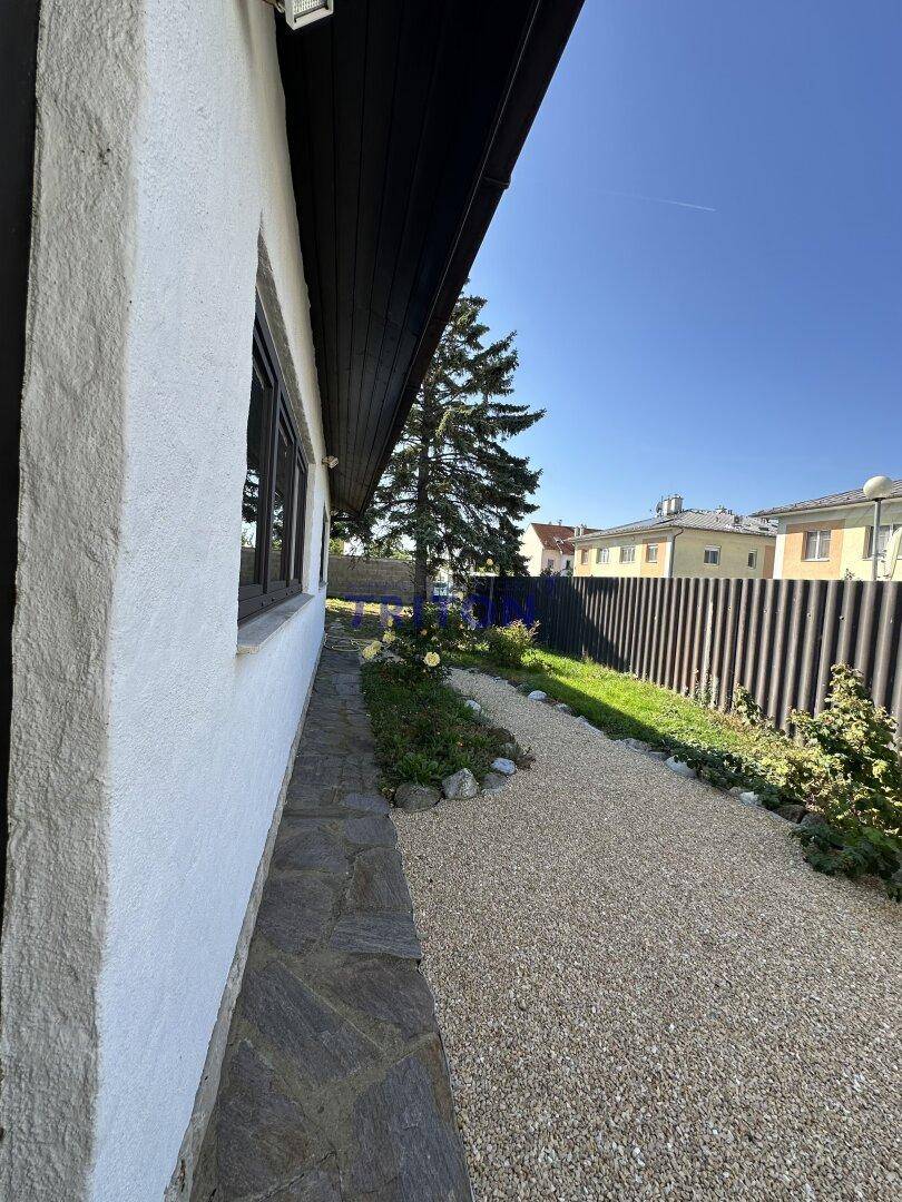 Seitenansicht des Hauses mit Kiesweg, Blumenbeeten und Zaun.