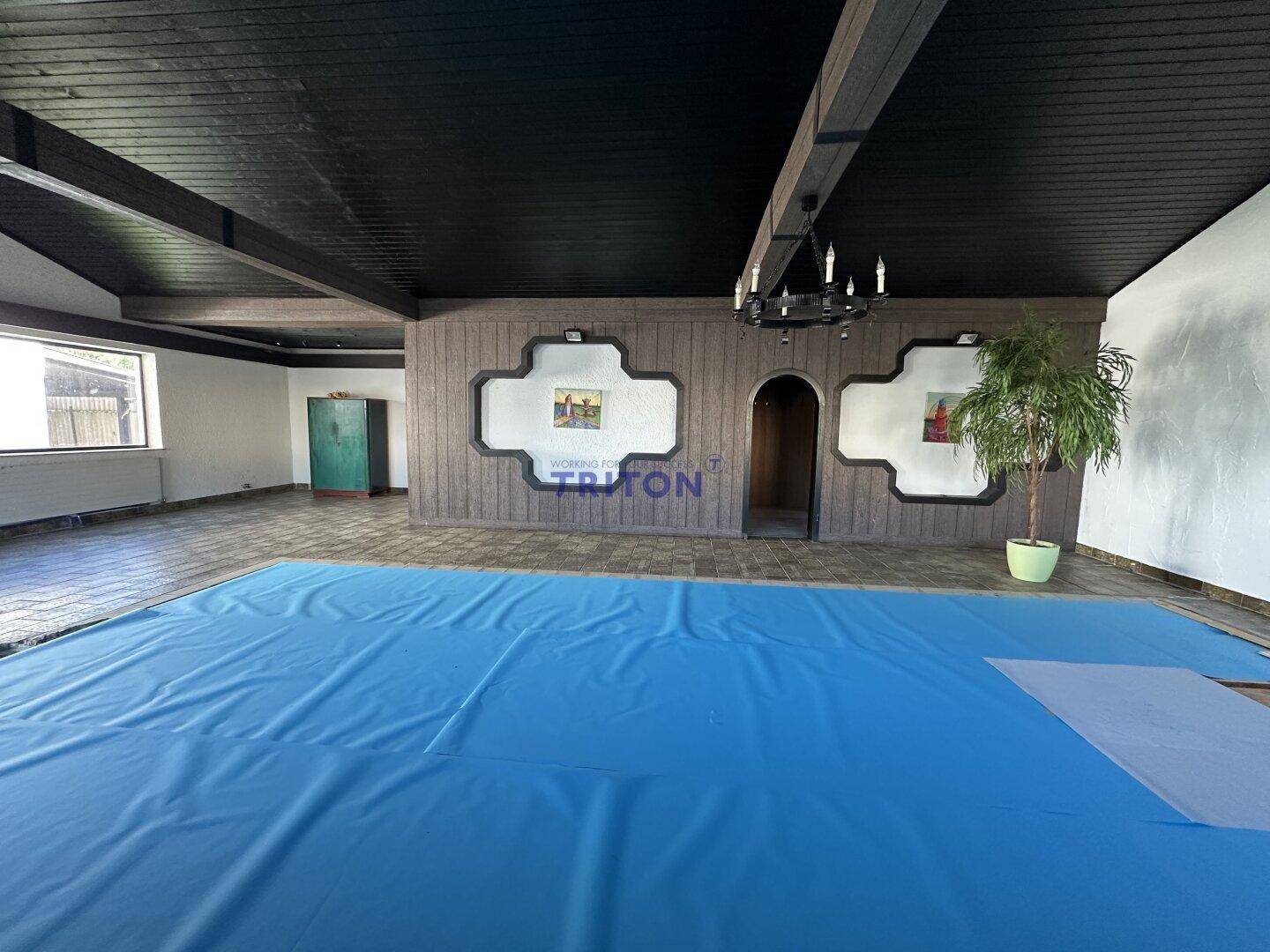 Innenraum mit abgedecktem Pool, dunkler Holzdecke und dekorativer Holzvertäfelung an der Wand.