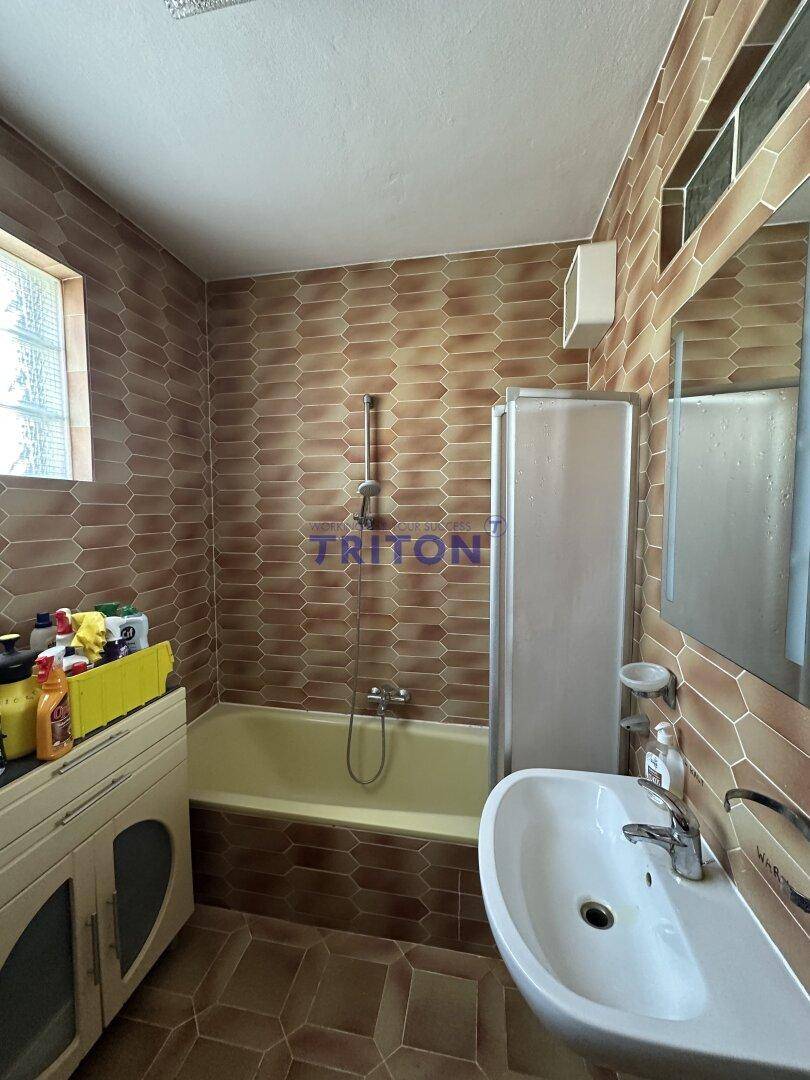 Badezimmer mit braunen Fliesen, Badewanne mit Duschvorrichtung und Einzelwaschbecken.
