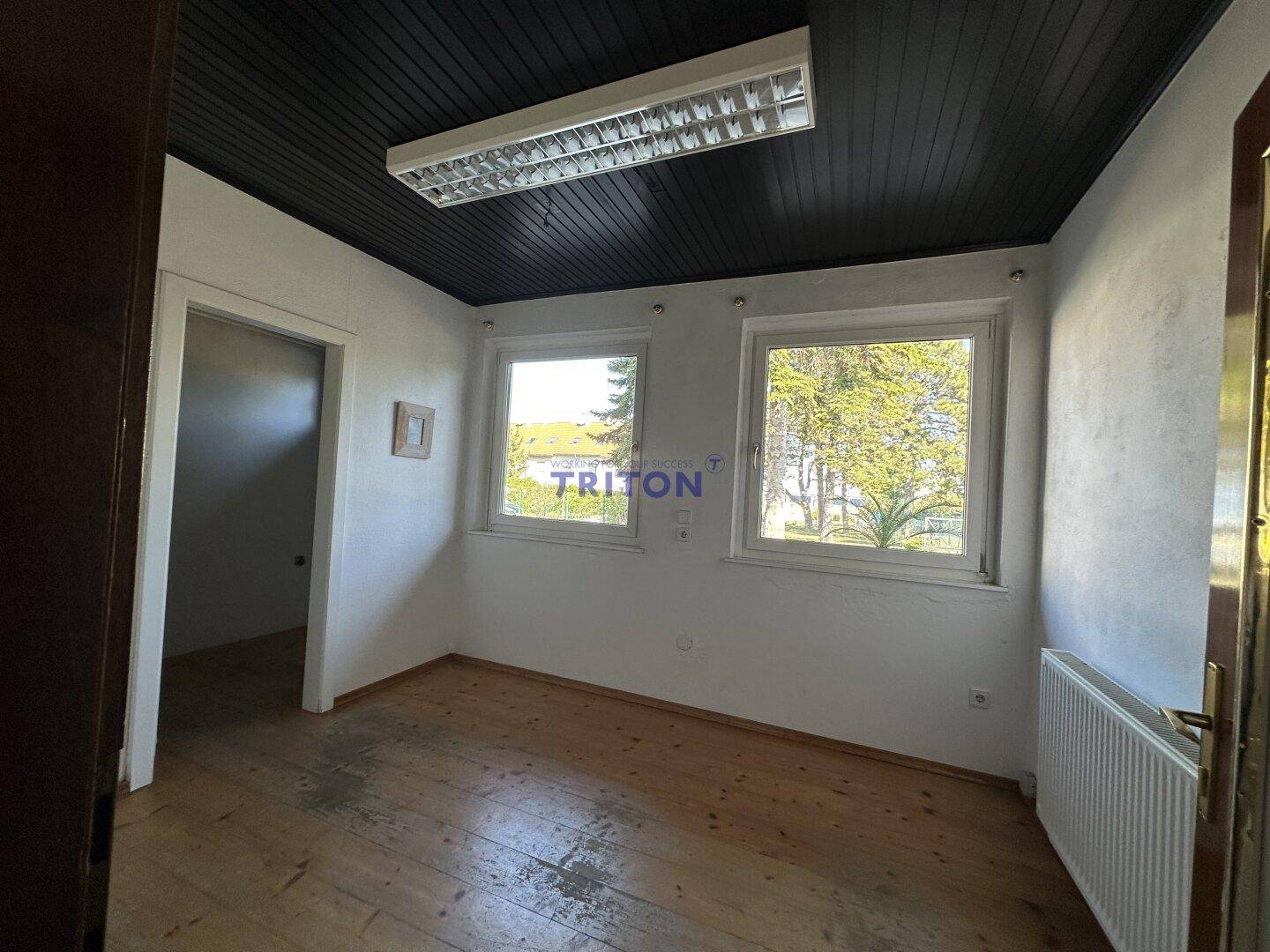 Heller Raum mit Holzfußboden, dunkler Holzdecke und zwei Fenstern.