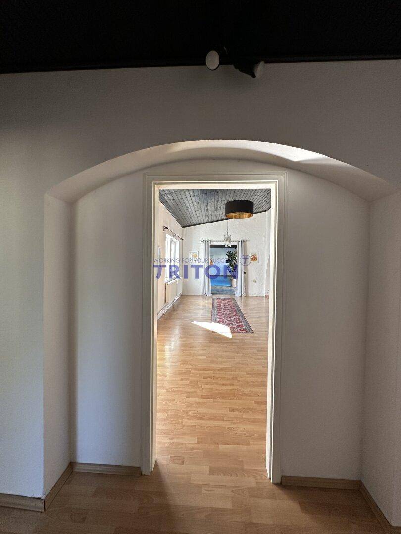 Blick durch einen Torbogen in einen hellen Raum mit Holzfußboden.