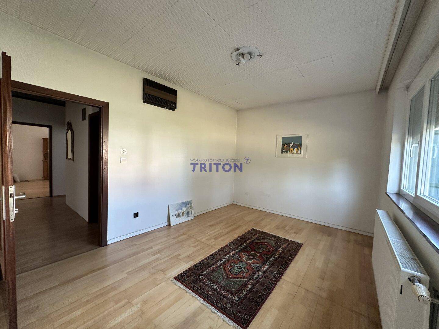 Heller Raum mit Holzfußboden, strukturierter Decke und einem Fenster.