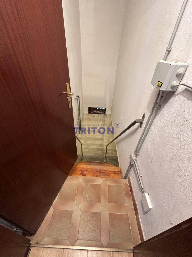 Treppenabgang in den Keller mit Fliesenstufen und sichtbaren Installationen.