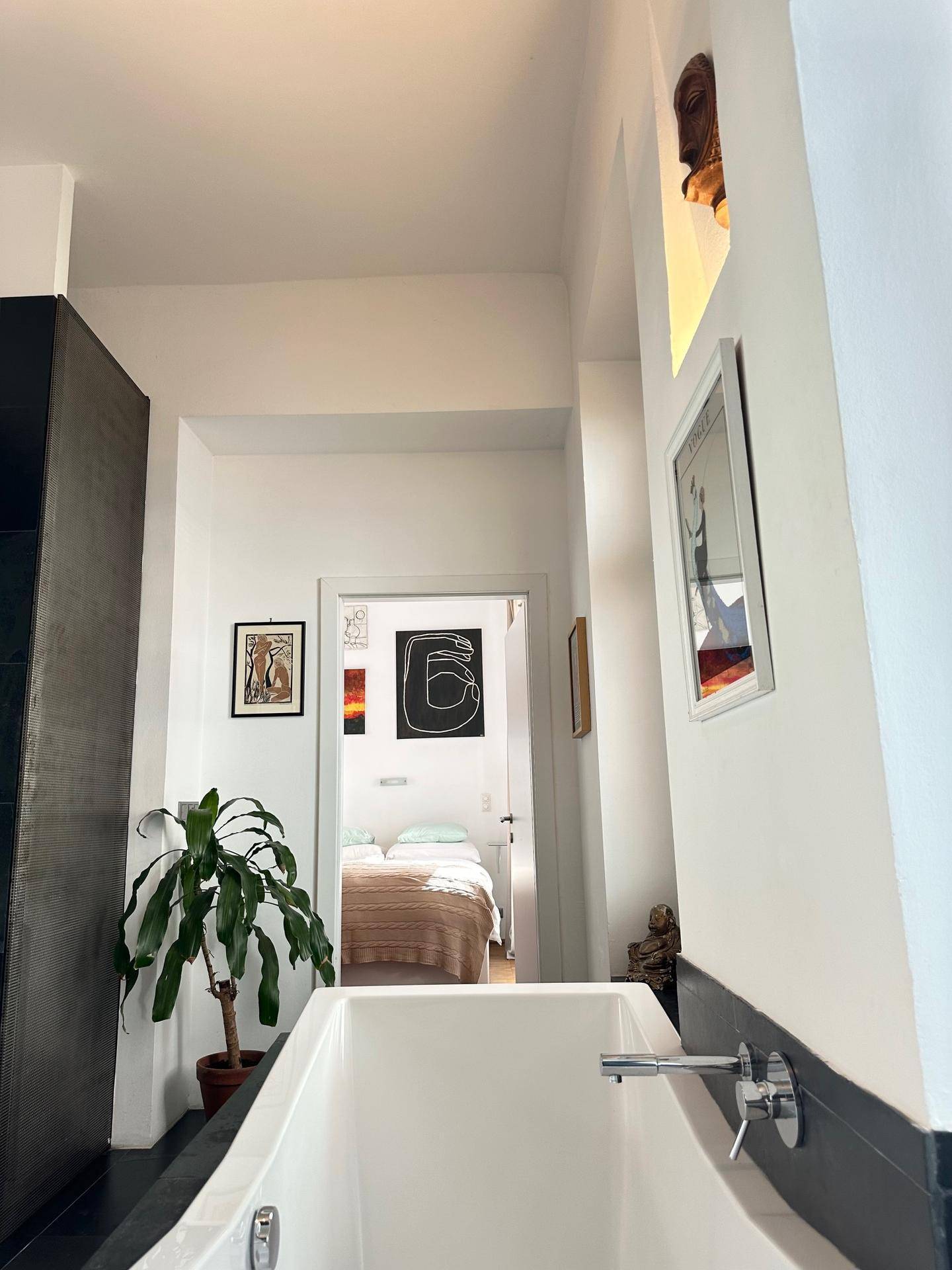 Blick aus dem modernen Badezimmer mit Badewanne in ein helles Schlafzimmer.