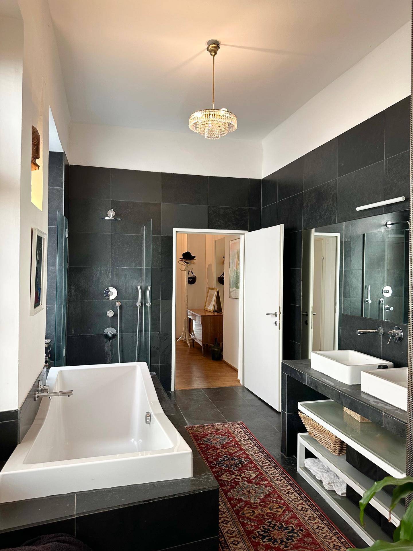 Modernes Badezimmer mit dunklen Fliesen, einer Badewanne und zwei Waschbecken.