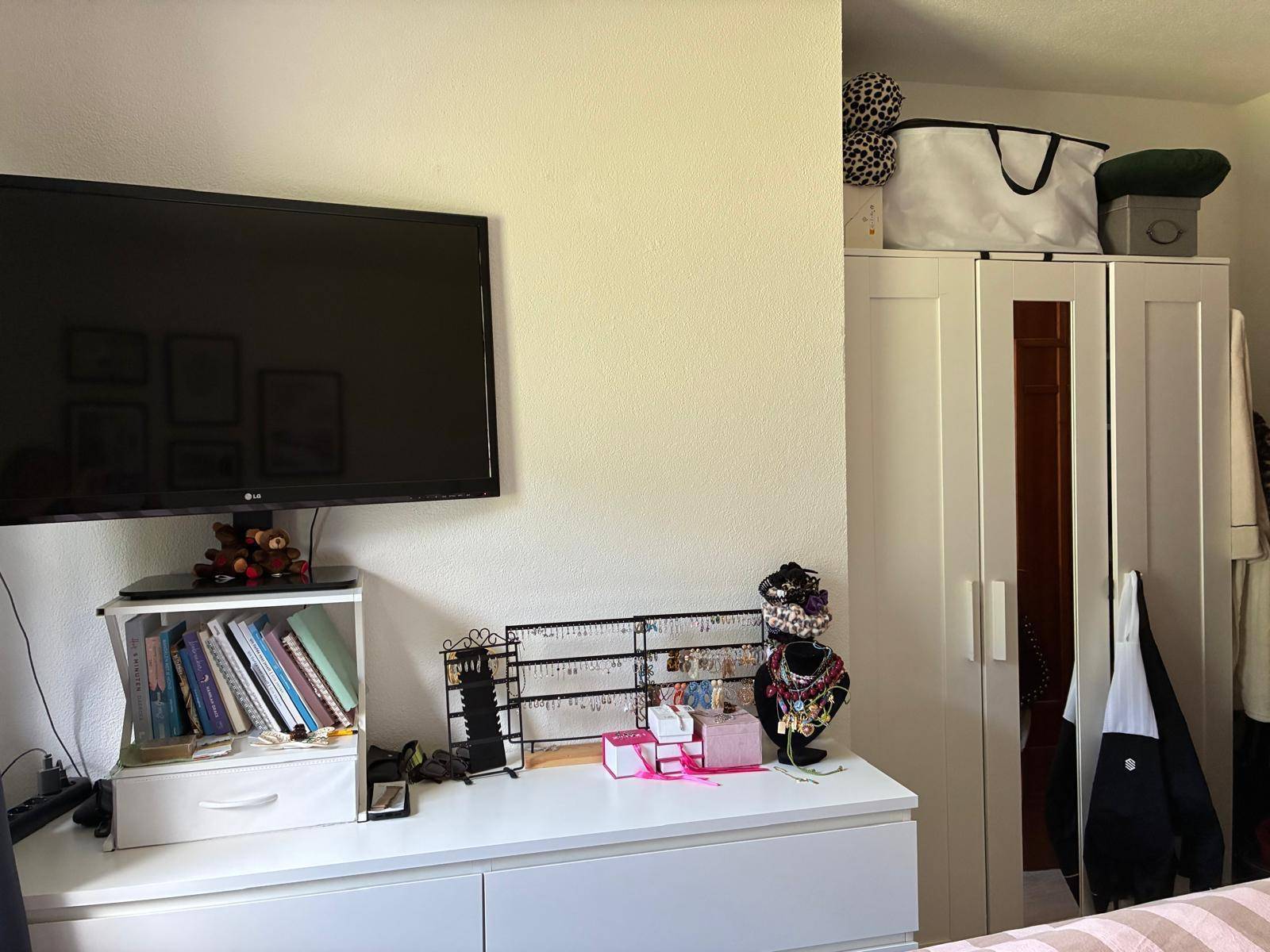 Bereich im Schlafzimmer mit wandmontiertem Fernseher, Kommode und einem weißen Kleiderschrank.