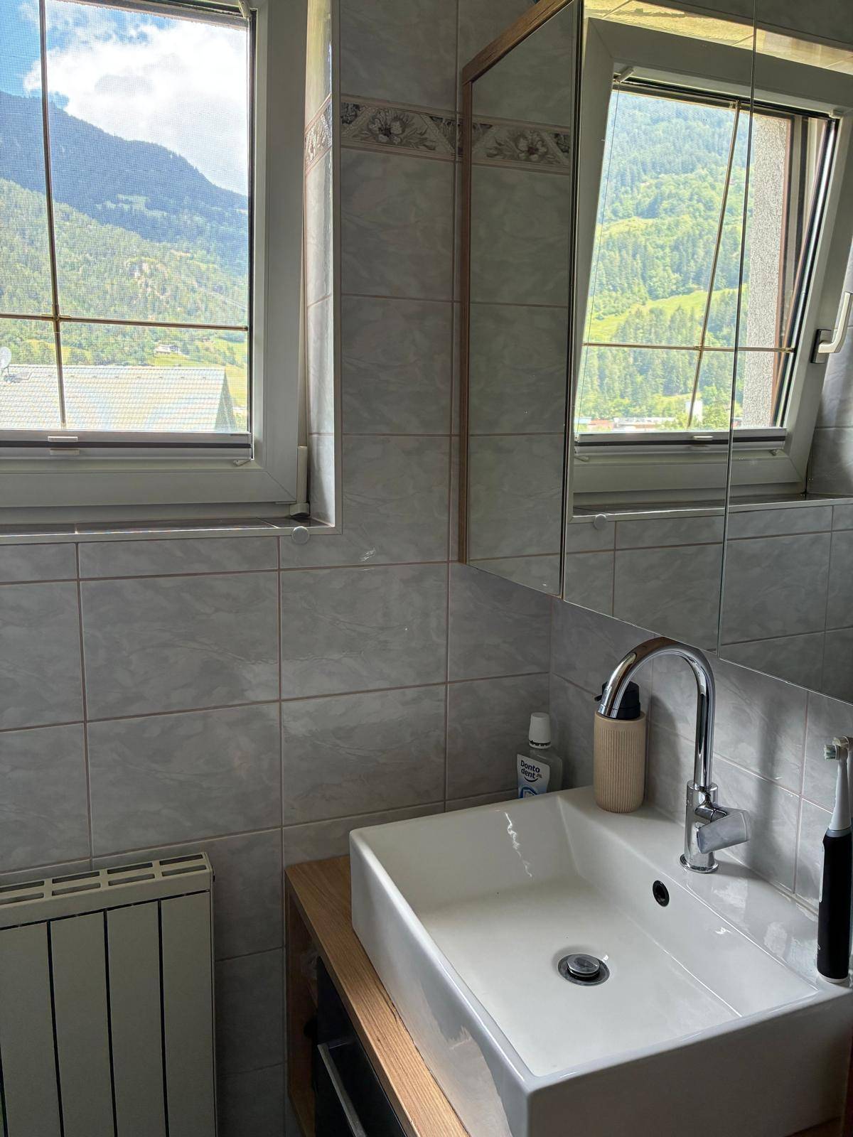 Badezimmer mit modernem Waschbecken, Spiegelschrank und einem Fenster mit Bergblick.