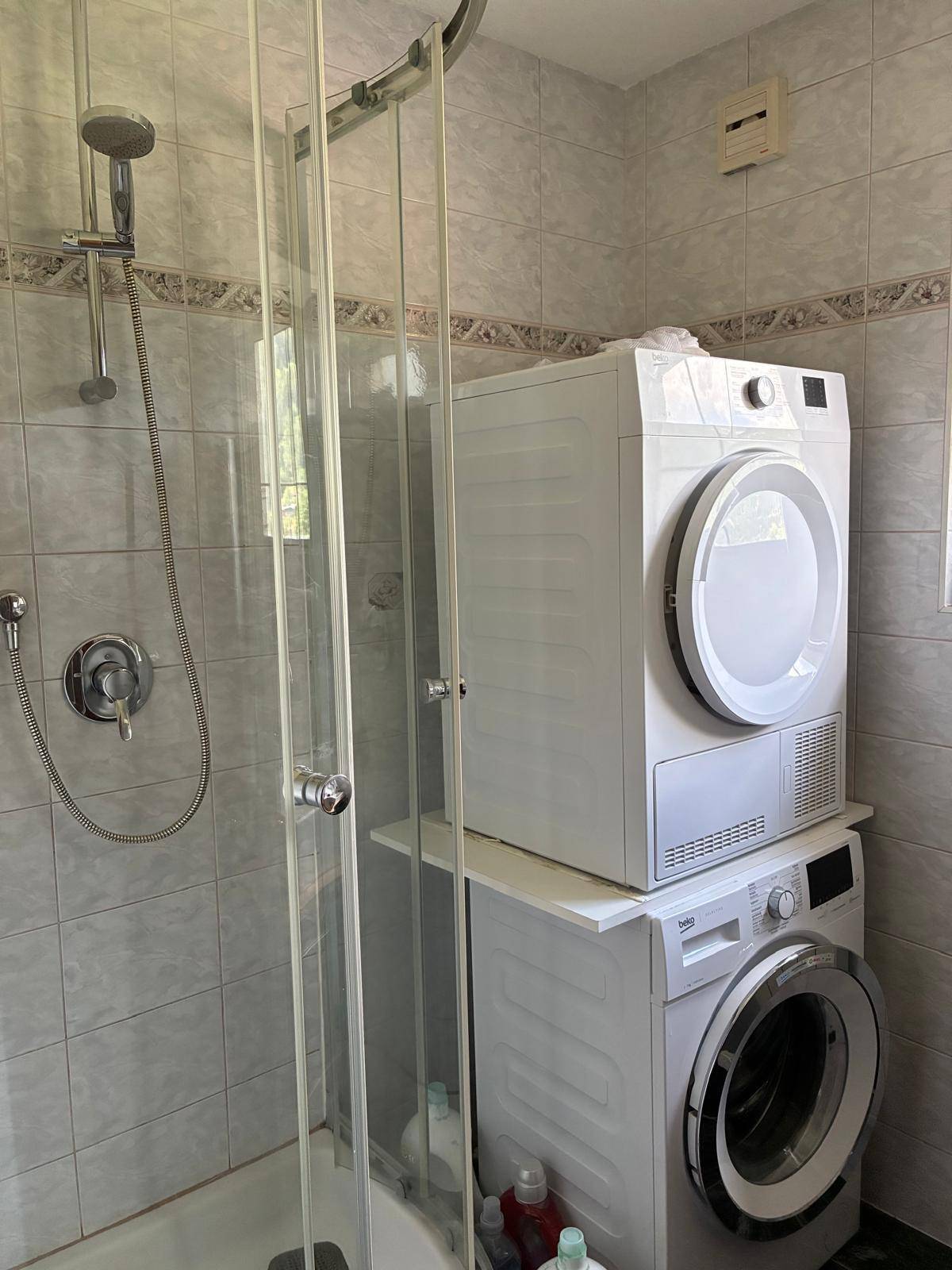 Duschbereich im Badezimmer mit gestapelter Waschmaschine und Trockner.