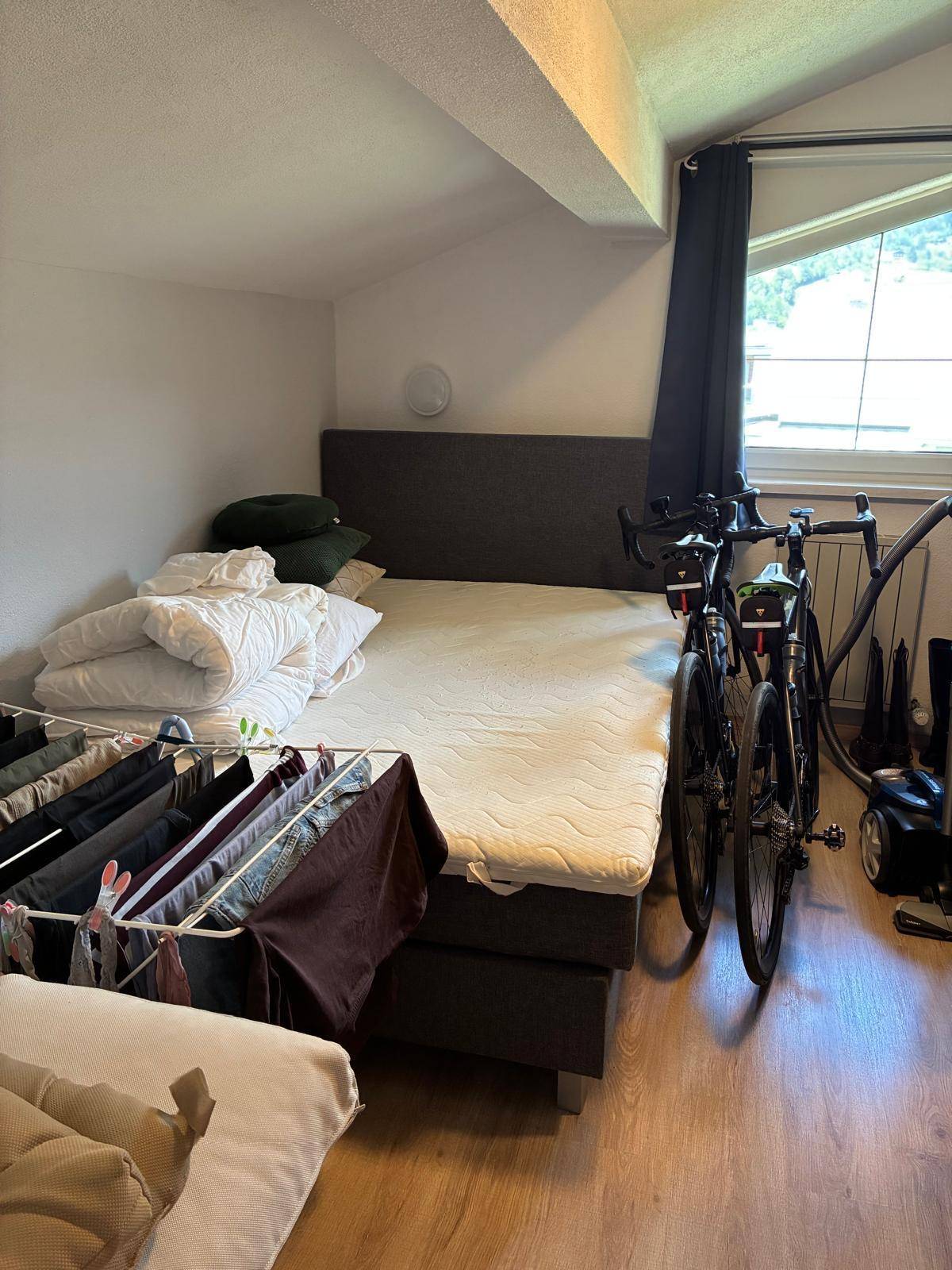 Schlafzimmer im Dachgeschoss mit Bett, Fahrrad und einem Wäscheständer, unter einer Dachschräge.