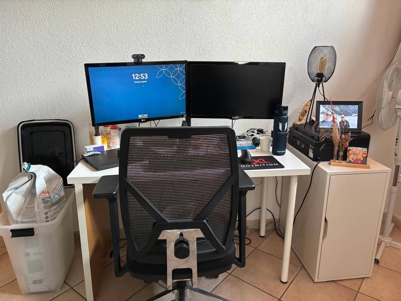 Funktionaler Heimbüro-Arbeitsplatz mit zwei Monitoren, ergonomischem Stuhl und einem weißen Schreibtisch.