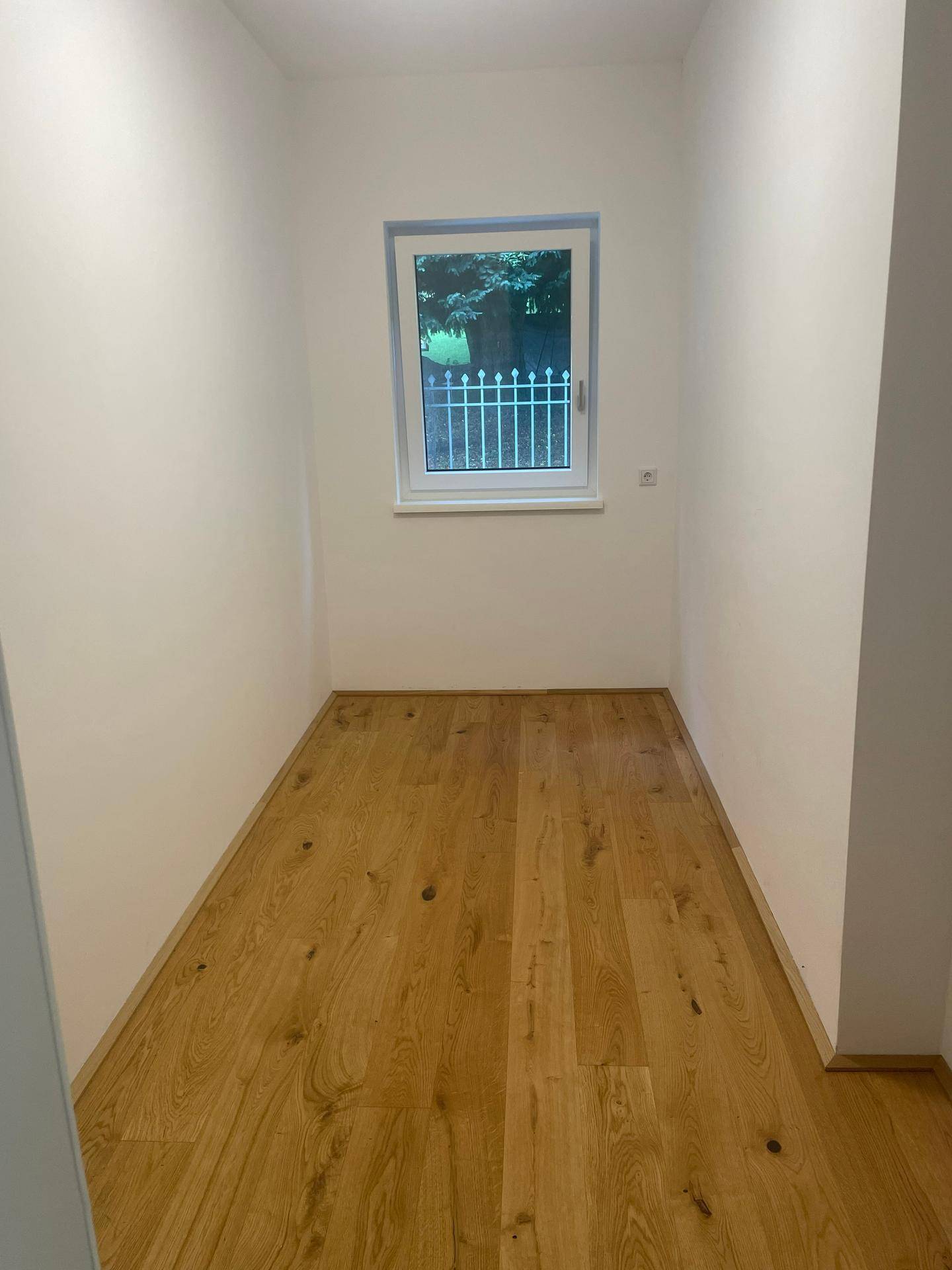 Schmaler Abstellraum mit Holzboden und einem Fenster, das Tageslicht hereinlässt.