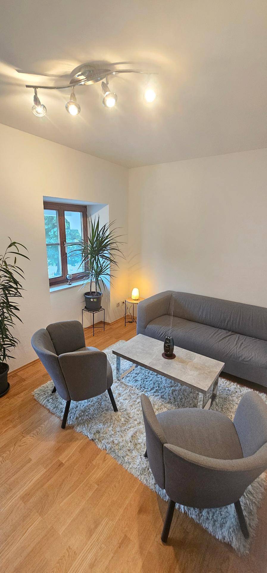 Komfortabler Wohnbereich mit Sofa, Sesseln und viel Tageslicht durch das große Fenster.