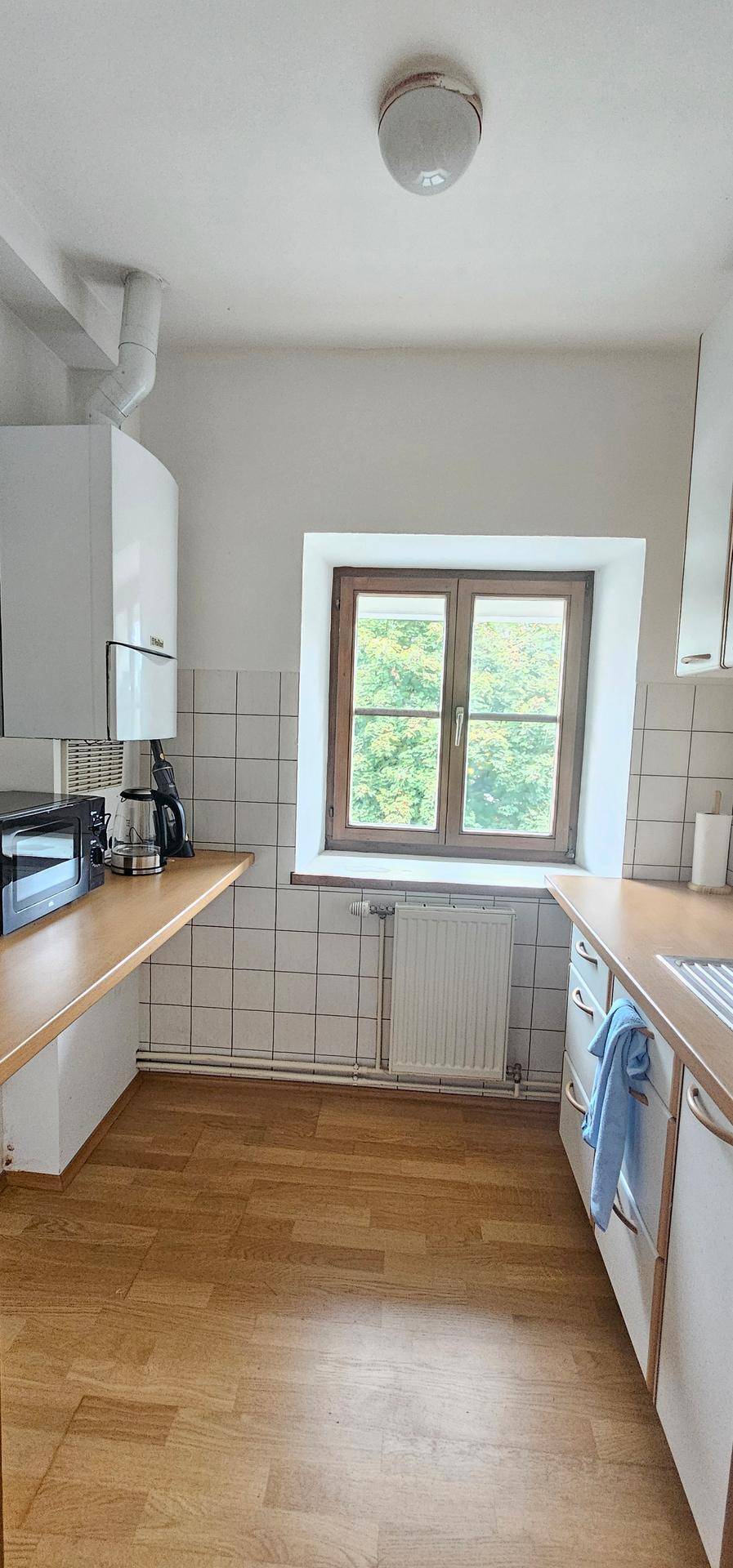 Funktionale Küche mit Holztheke, weißen Schränken und Fenster mit Blick ins Grüne.