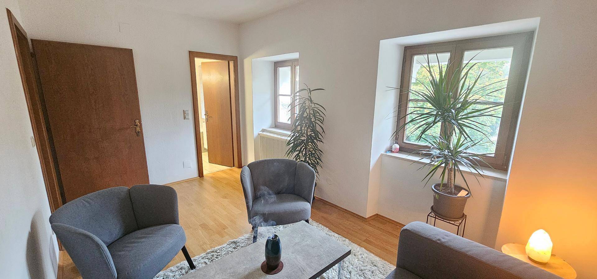Heller Wohnbereich mit zwei Sesseln, Couchtisch und Blick auf die Natur durch das Fenster.