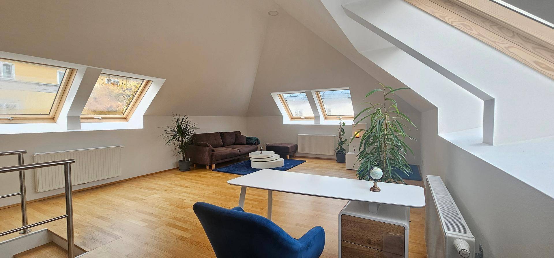 Geräumiger Dachgeschoss-Wohnbereich mit Sofa, Schreibtisch und mehreren Dachfenstern.