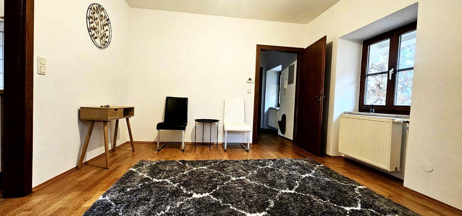 Gemütlicher Wohnbereich mit Holzboden, Teppich und einem Fenster mit Blick ins Grüne.
